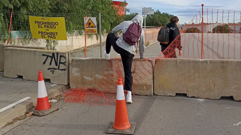 Dos joves salten les balisses que impedeixen el pas a peu pel pont entre el Mas Blau i el nucli urbà